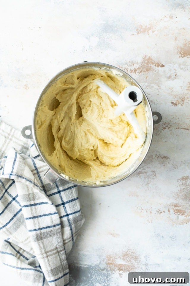 Overhead view of almond loaf batter in a mixing bowl being combined with an electric mixer.