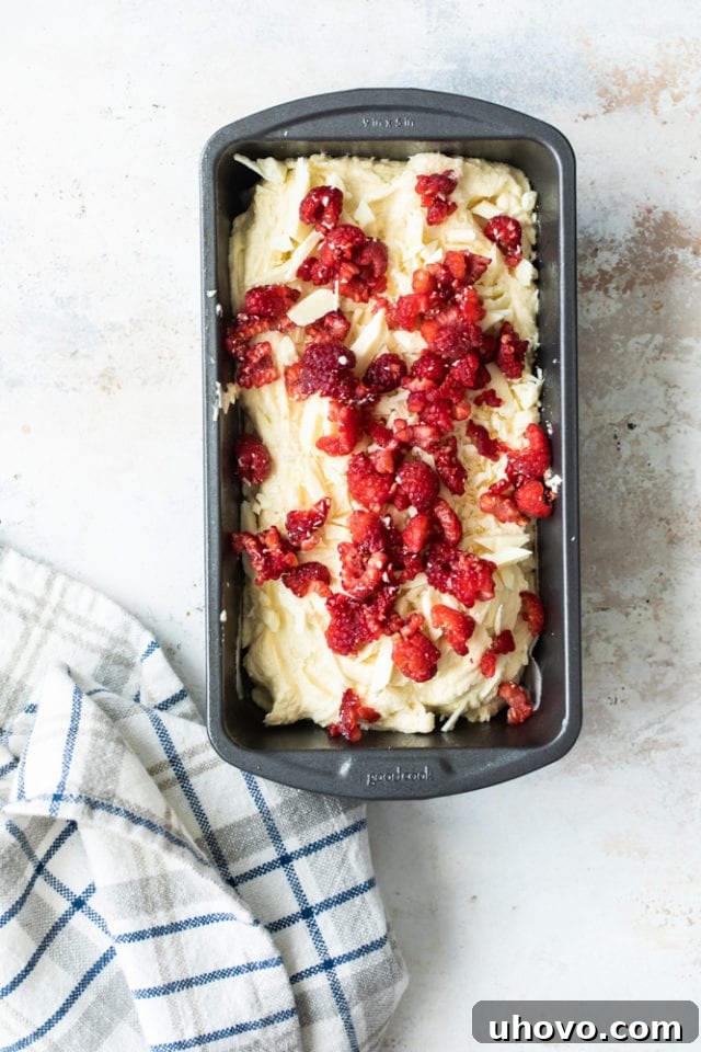 Almond bread batter in a pan with raspberries and white chocolate scattered over the top before baking.