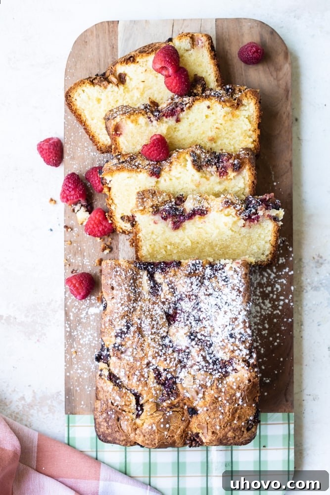 Raspberry white chocolate almond bread cooling on a wooden cutting board with a slice already removed.