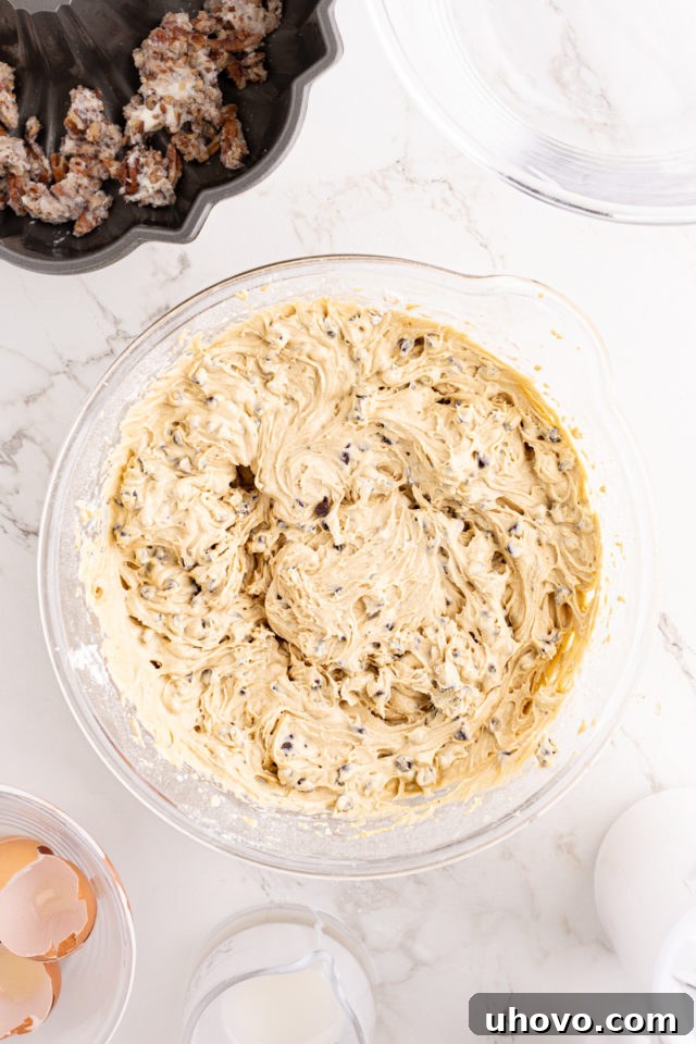 An overhead shot of the finished chocolate chip Bundt cake batter, now with chocolate chips, in a glass mixing bowl.