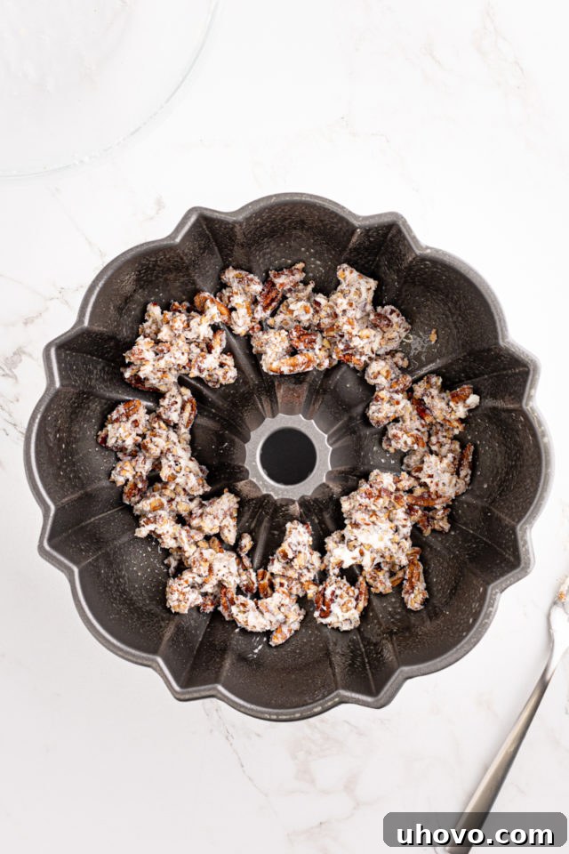 An overhead view showing the nutty topping mixture evenly spread in the bottom of a Bundt pan, ready for the cake batter.