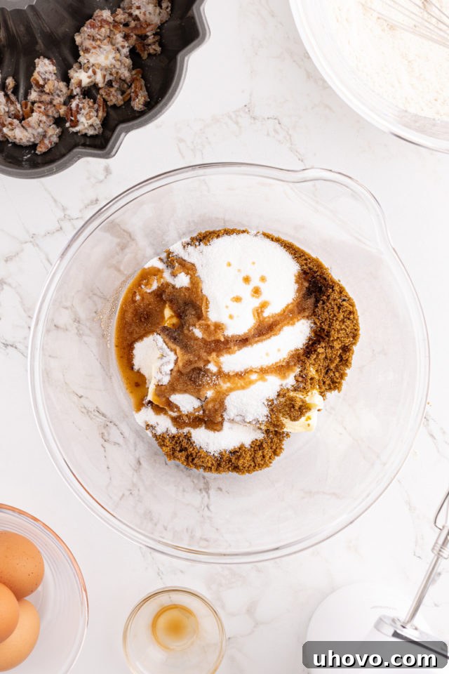 An overhead shot revealing butter, granulated sugar, brown sugar, and vanilla extract creaming together in a glass mixing bowl.