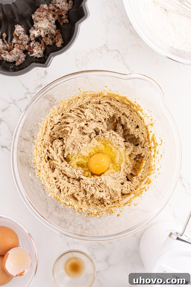 An overhead view captures an egg being added to the creamy mixture of butter and sugar, preparing for the next step.