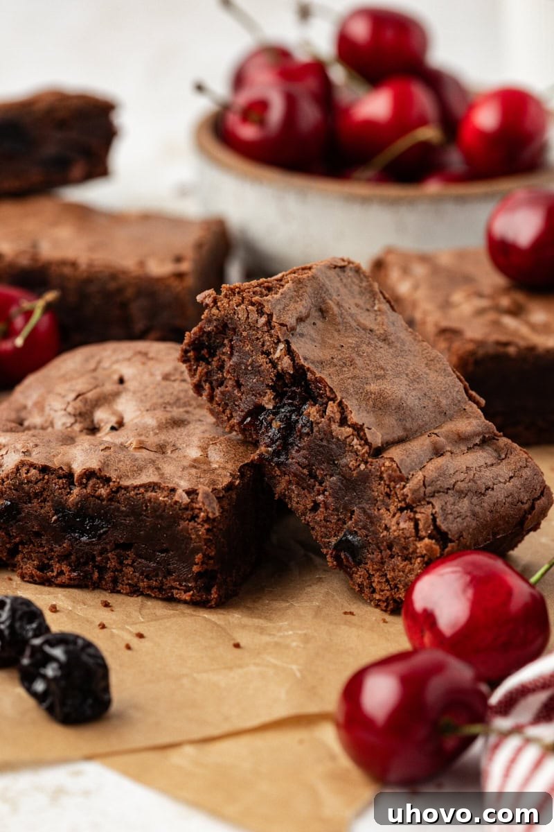 Dark chocolate sour cherry brownies stacked on parchment paper, ready to be served or stored.