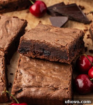 Dark chocolate sour cherry brownies on parchment paper, freshly baked and cut into squares.