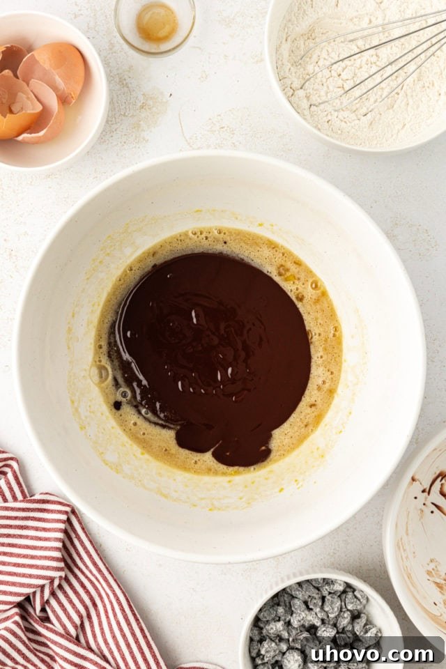 Melted chocolate and butter mixture being poured into the bowl of wet ingredients (sugar, eggs, vanilla) for brownie batter.