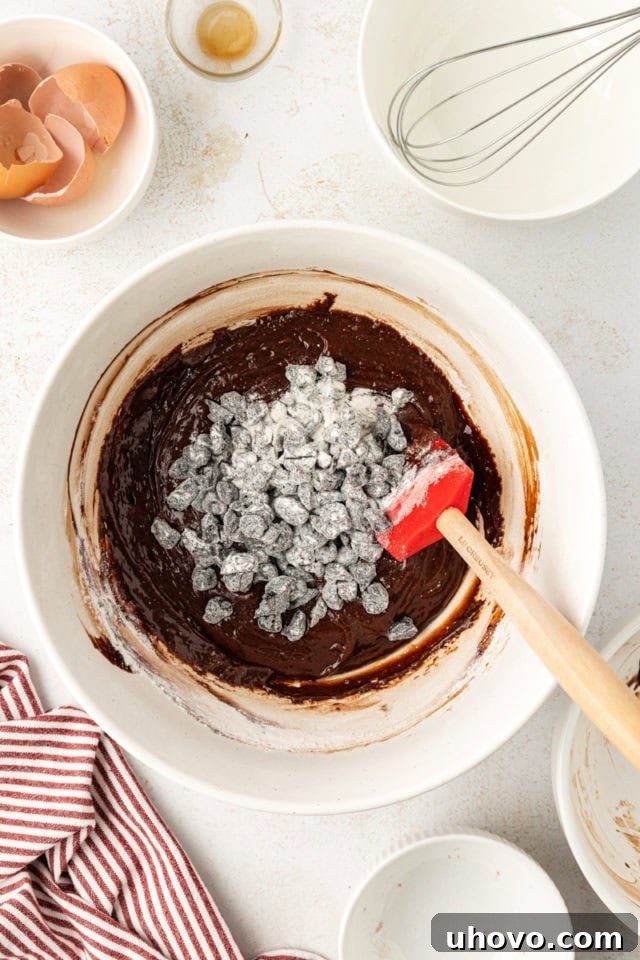 Flour-coated dried cherries being folded into the dark chocolate brownie batter with a spatula.