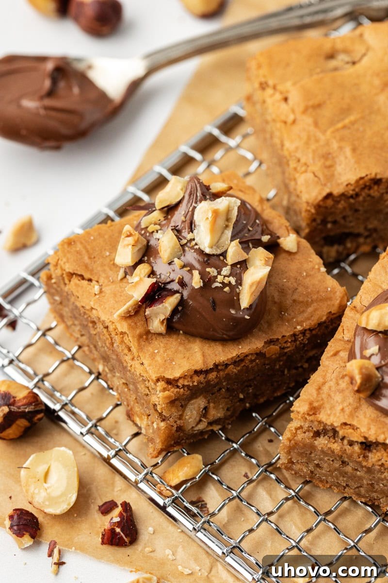 A single, perfectly cut hazelnut blondie rests on a wire cooling rack, with more delicious blondies blurred in the background, highlighting its rich, fudgy interior.