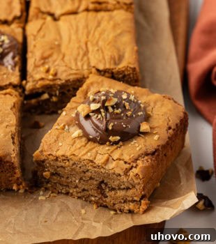 A delectable hazelnut blondie shown on a cutting board with more blondies in the background, enticing viewers with its rich appearance.