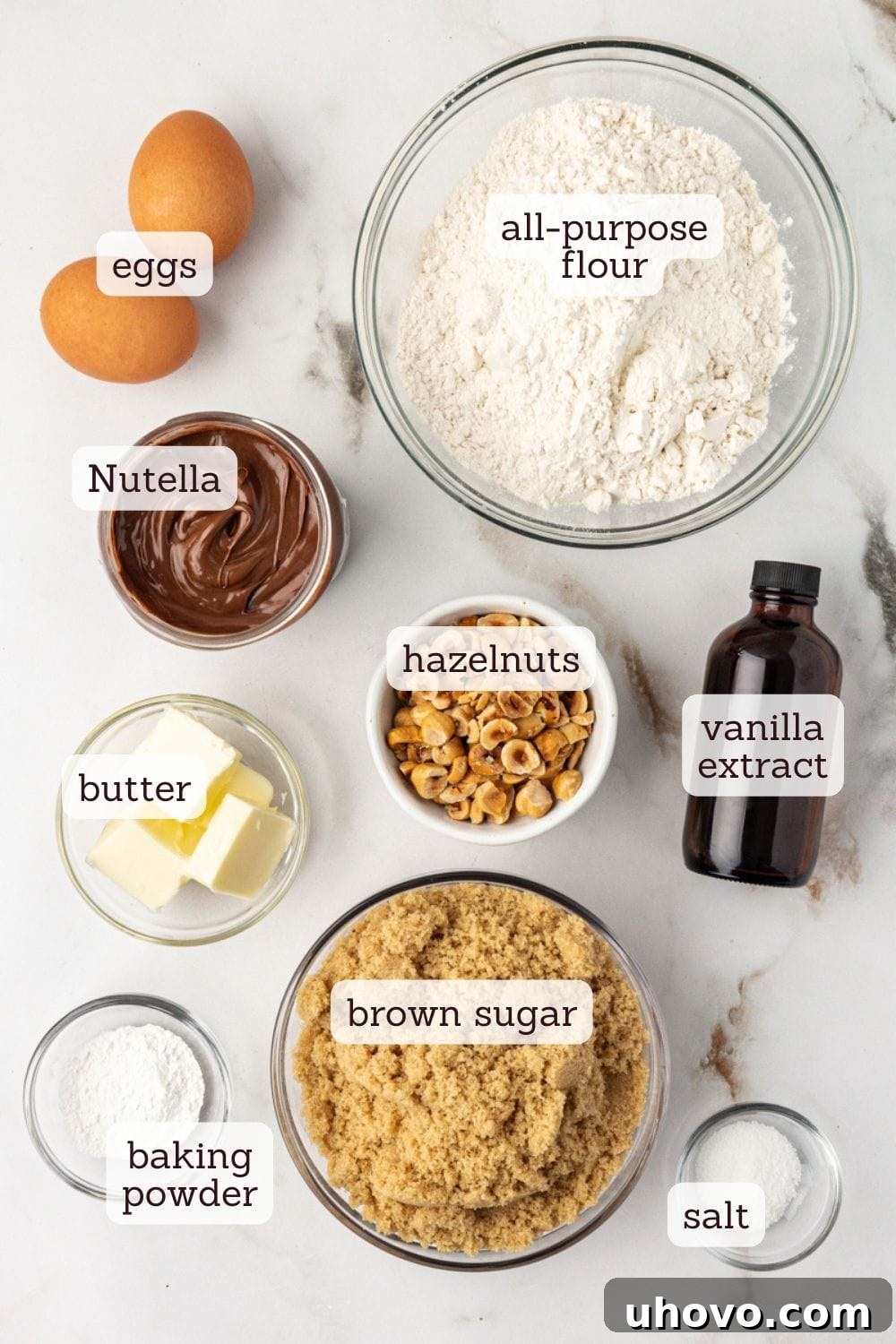 An overhead shot showcasing all the essential ingredients laid out for making hazelnut blondies, including flour, sugar, butter, eggs, hazelnuts, and Nutella.