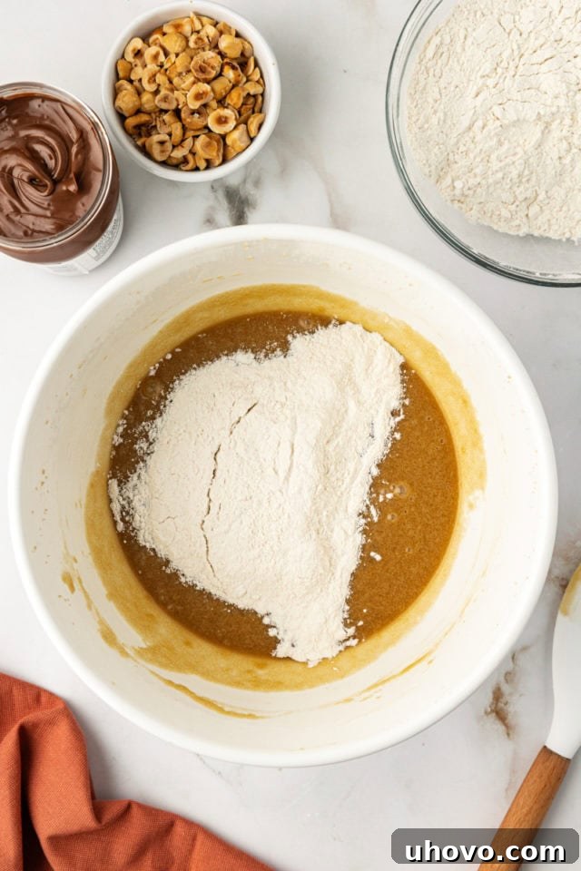 An overhead perspective showing the gradual addition of the whisked dry ingredients into the bowl of wet ingredients, illustrating the process of combining the blondie batter.