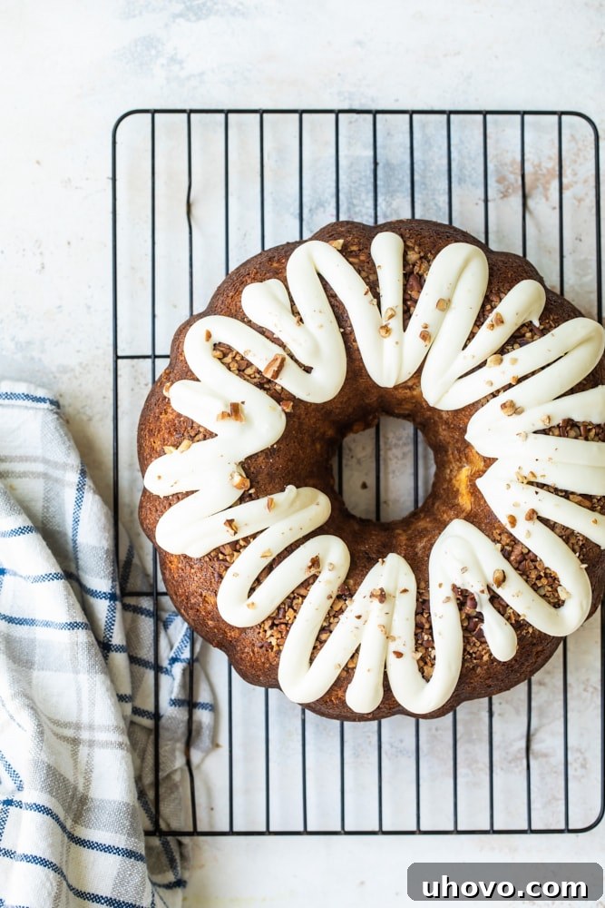 Whole hummingbird Bundt cake on wire rack with cream cheese glaze and pecans