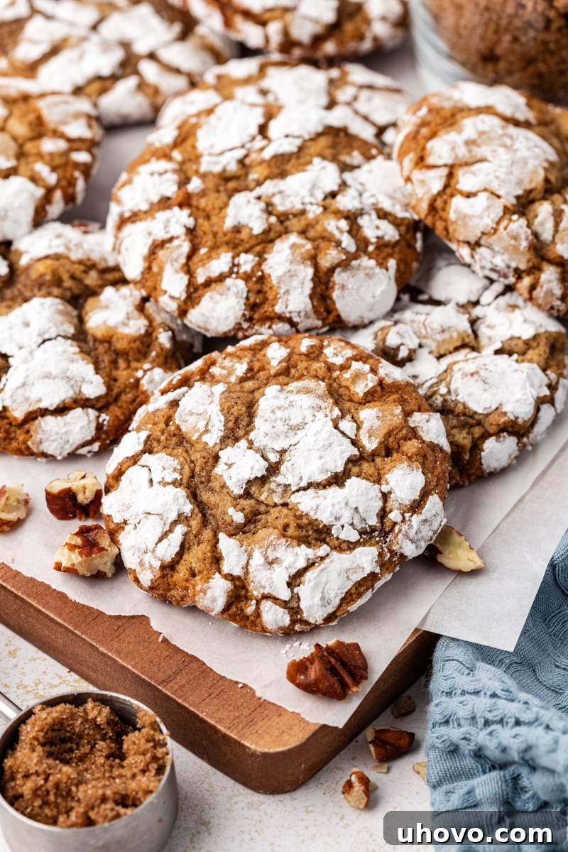 A stack of golden brown sugar crinkle cookies resting on a parchment-lined wooden board, dusted with powdered sugar.