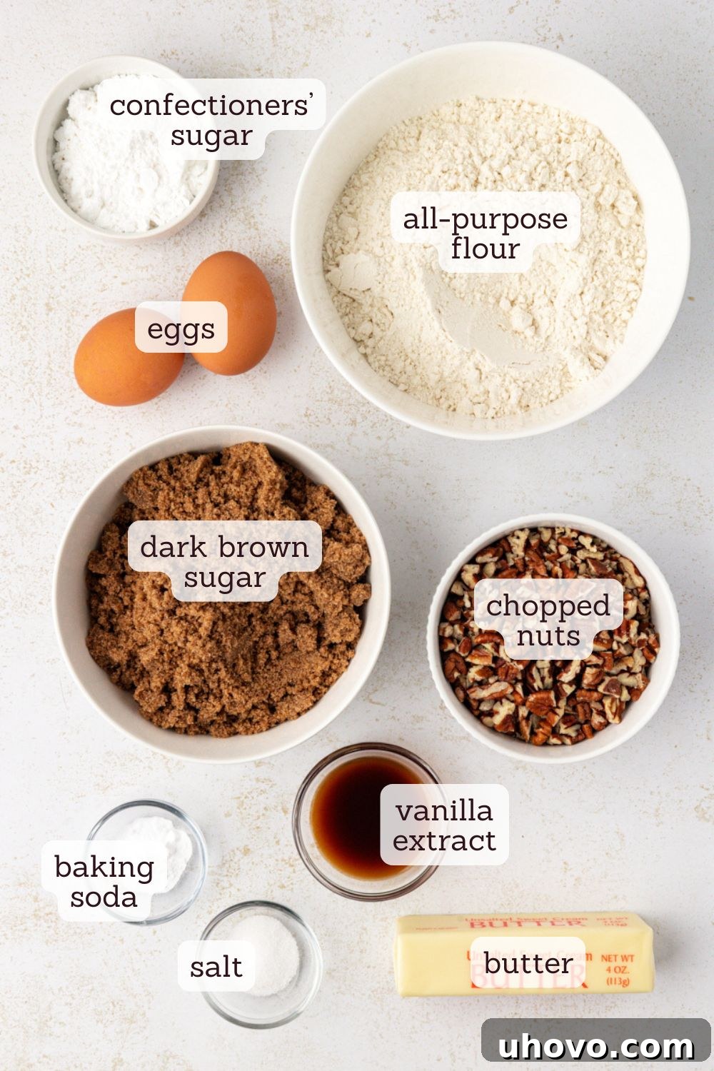 Overhead view of ingredients for brown sugar crinkle cookies, neatly arranged and labeled, including dark brown sugar, butter, eggs, flour, and pecans.