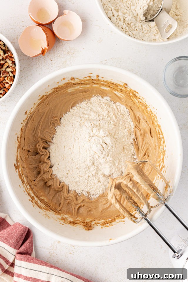 Dry ingredients, specifically flour, being gradually added to the wet cookie dough mixture in a stand mixer.