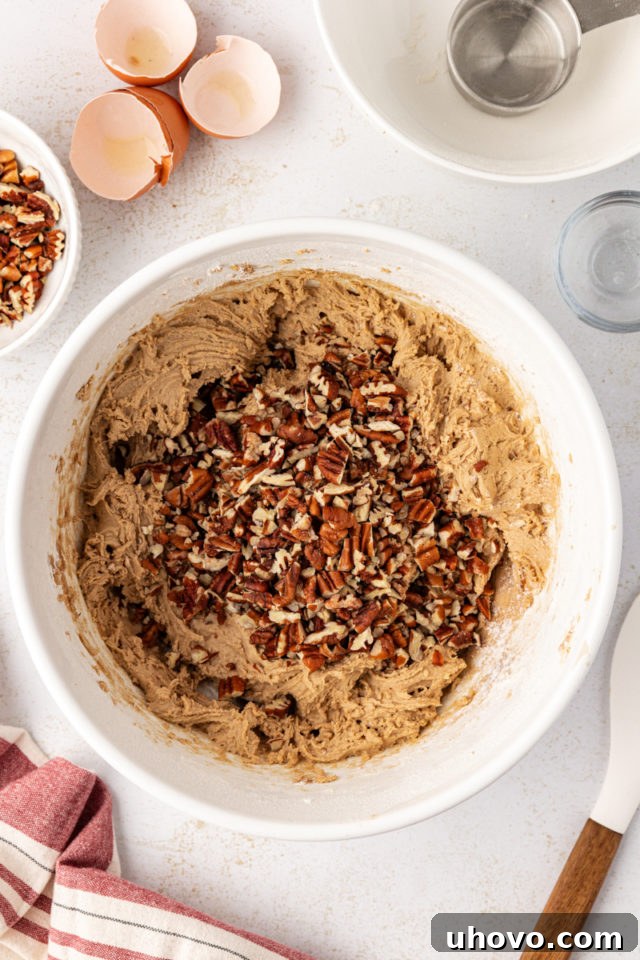 Chopped pecans being folded into a bowl of brown sugar cookie dough, ensuring even distribution.