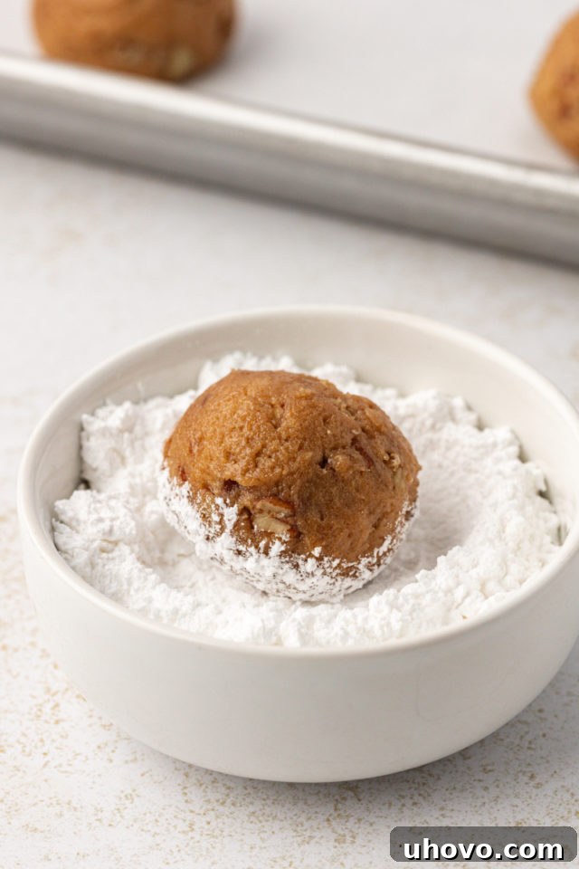 A brown sugar cookie dough ball being thoroughly rolled in a dish of powdered sugar to create the crinkle effect.