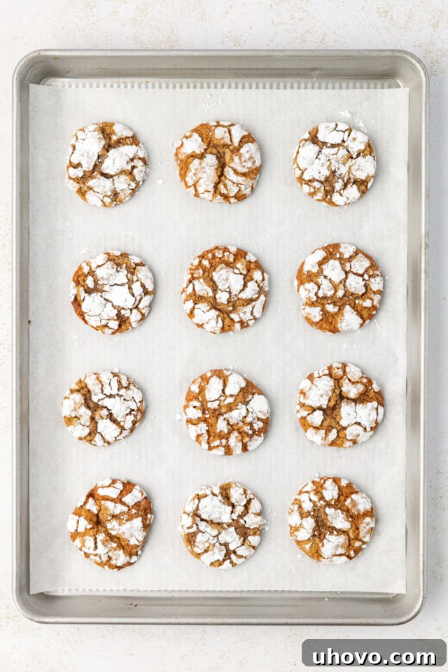An overhead view of brown sugar crinkle cookies baking on a parchment-lined baking sheet, showing their characteristic cracked tops.