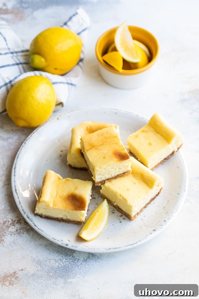 Stack of Limoncello Cheesecake Squares on a white plate, garnished with a lemon slice and zest
