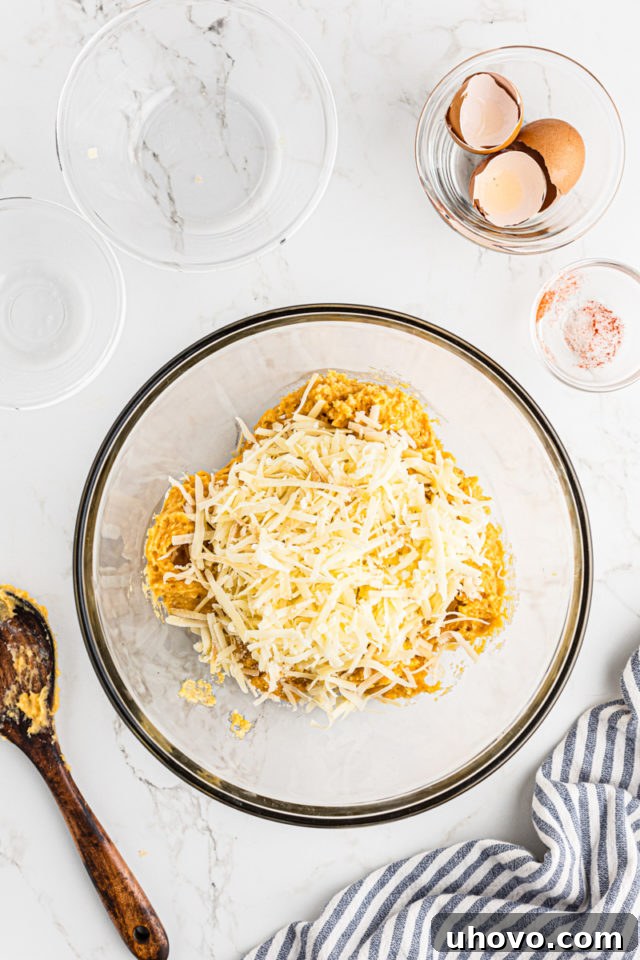 Overhead view of shredded Swiss and Parmesan cheeses being added to the prepared gougères dough in a glass mixing bowl.