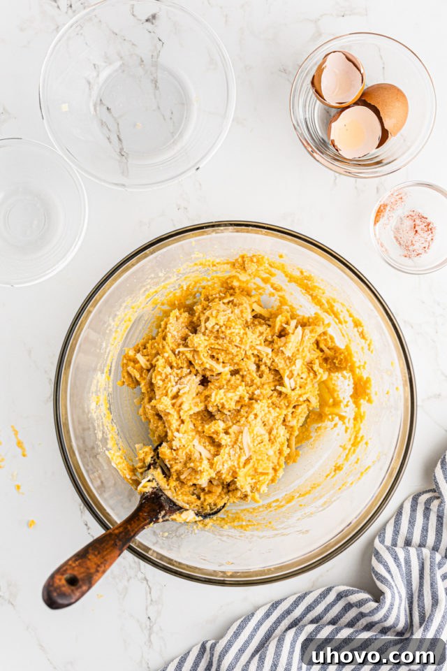 Overhead view of the fully mixed gougères dough with cheese folded in, resting in a glass bowl, ready for scooping.