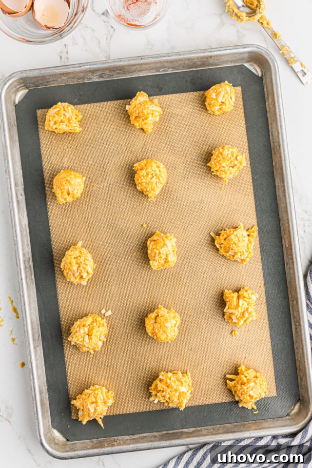 Overhead view of scoops of gougères dough neatly arranged on a silicone baking mat on a baking sheet, ready for the oven.