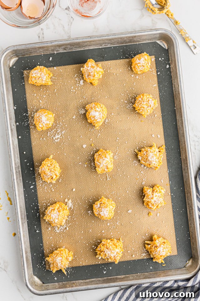 Overhead view of unbaked gougères on a silicone mat, with coarse salt and reserved Parmesan cheese sprinkled on top.