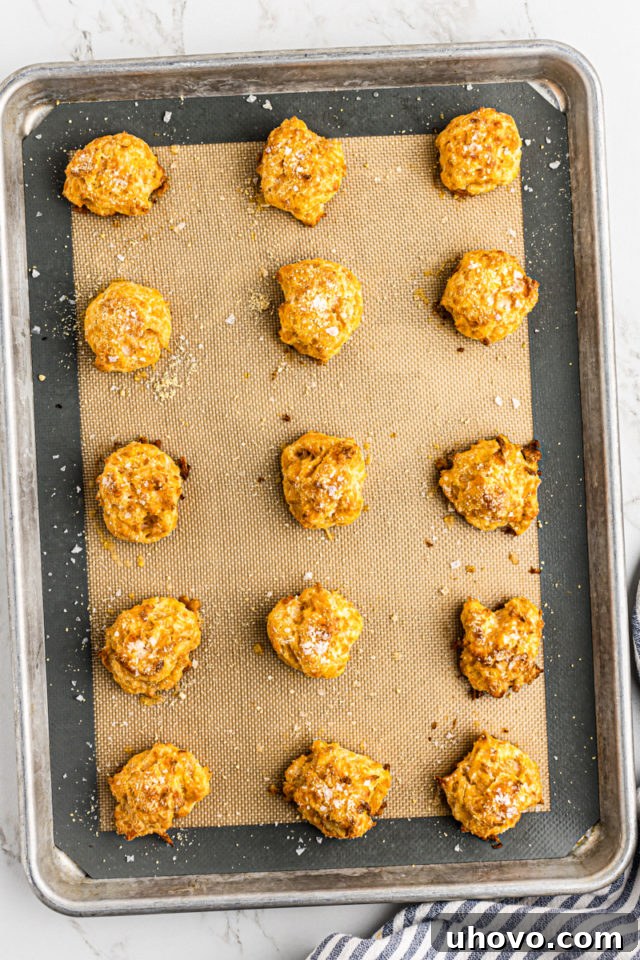 Overhead view of freshly baked, golden-brown gougères resting on a silicone baking mat, having puffed up perfectly.