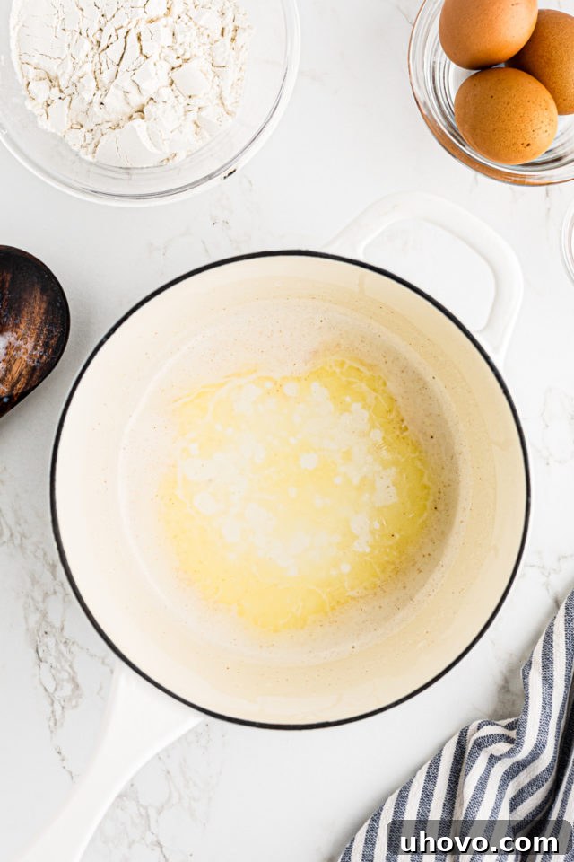 Overhead view of milk, butter, salt, and cayenne pepper being warmed in a saucepan on the stovetop.