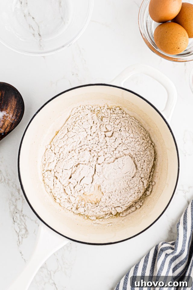 Overhead view of all-purpose flour being added to the hot milk and butter mixture in a saucepan.
