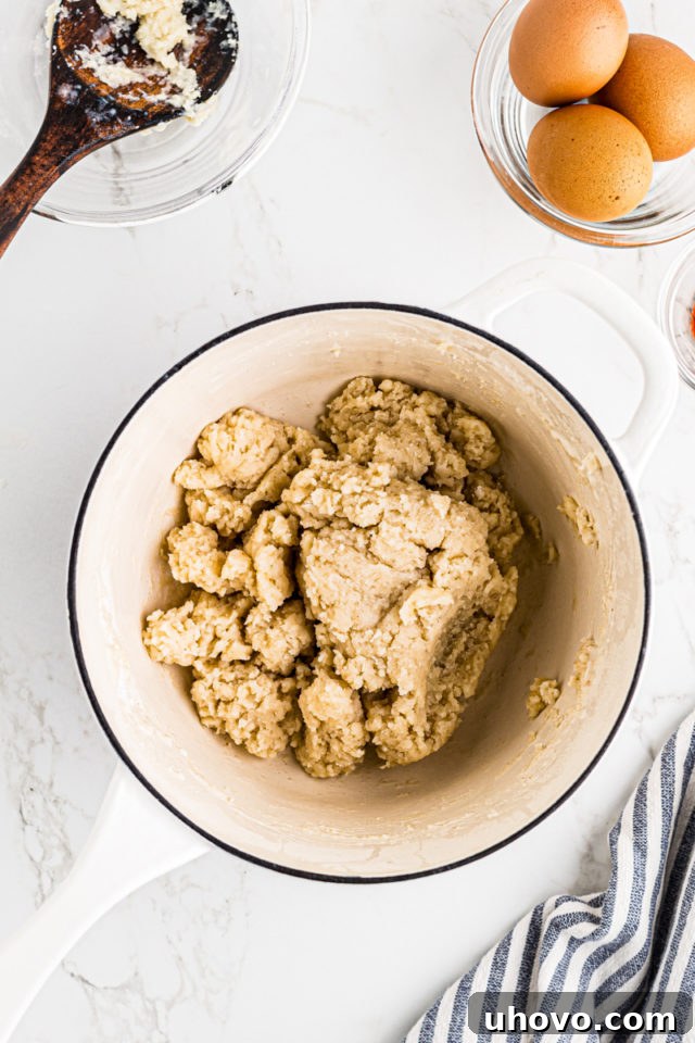 Overhead view of gougères dough in a pan, actively being stirred on the stovetop to dry it out.