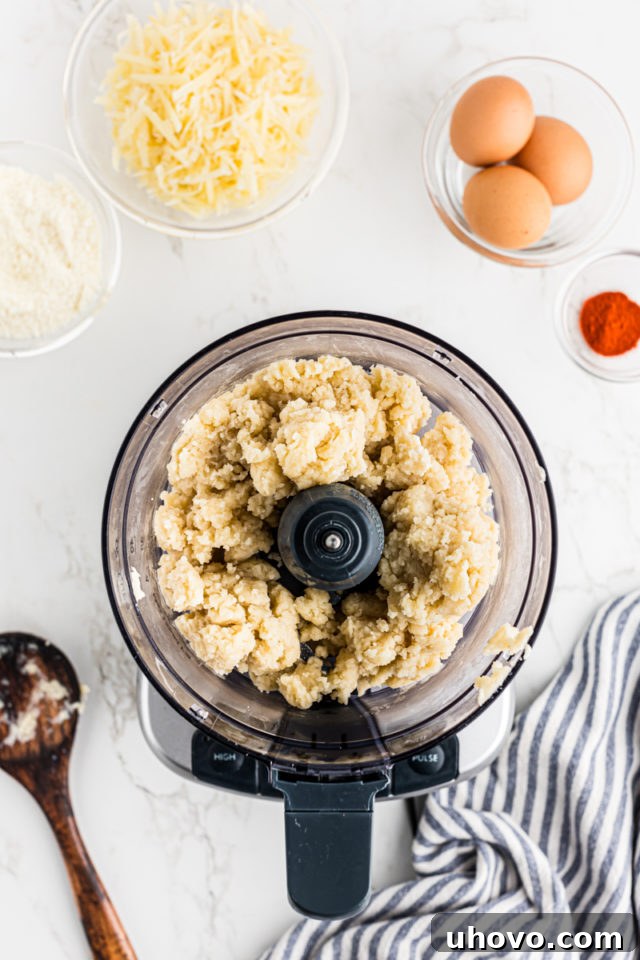 Overhead view of the gougères dough being transferred from the saucepan into a food processor for cooling and mixing.