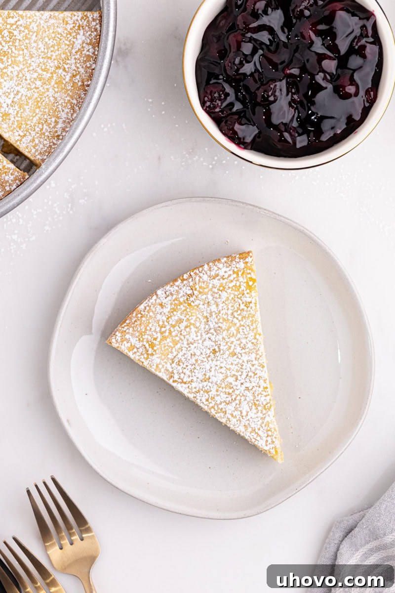 A perfect slice of Almond Gâteau Breton resting on a pristine white plate, showcasing its golden crust and dense, tender interior, ready to be enjoyed.