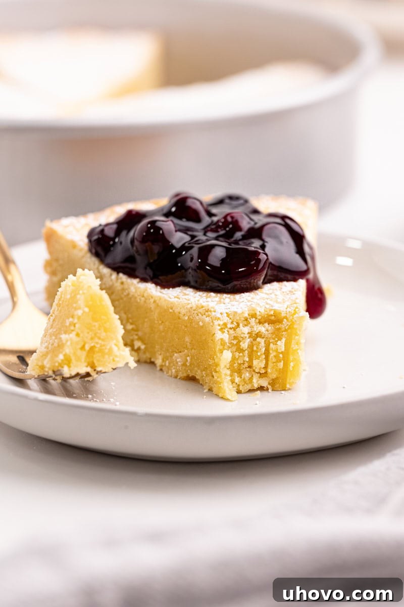 A delicious slice of Almond Gâteau Breton on a white plate, with a fork holding a perfect bite, highlighting the cake's tender interior and golden crust.