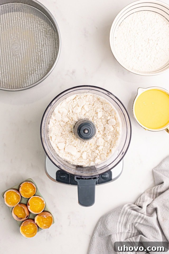 A close-up, overhead view of blanched almonds and granulated sugar being processed together in a food processor, creating a fine, aromatic mixture for the Gâteau Breton batter.