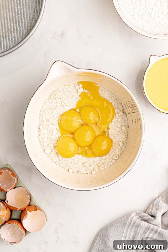 An overhead shot showing rich egg yolks being added to the finely ground almond and sugar mixture in a mixing bowl, ready to be incorporated.