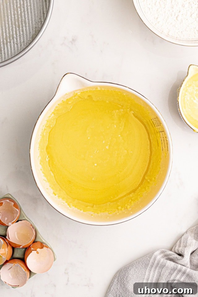 Melted, golden butter being slowly poured into the creamy mixture of ground almonds, sugar, and egg yolks, ready to be blended into the rich cake batter.