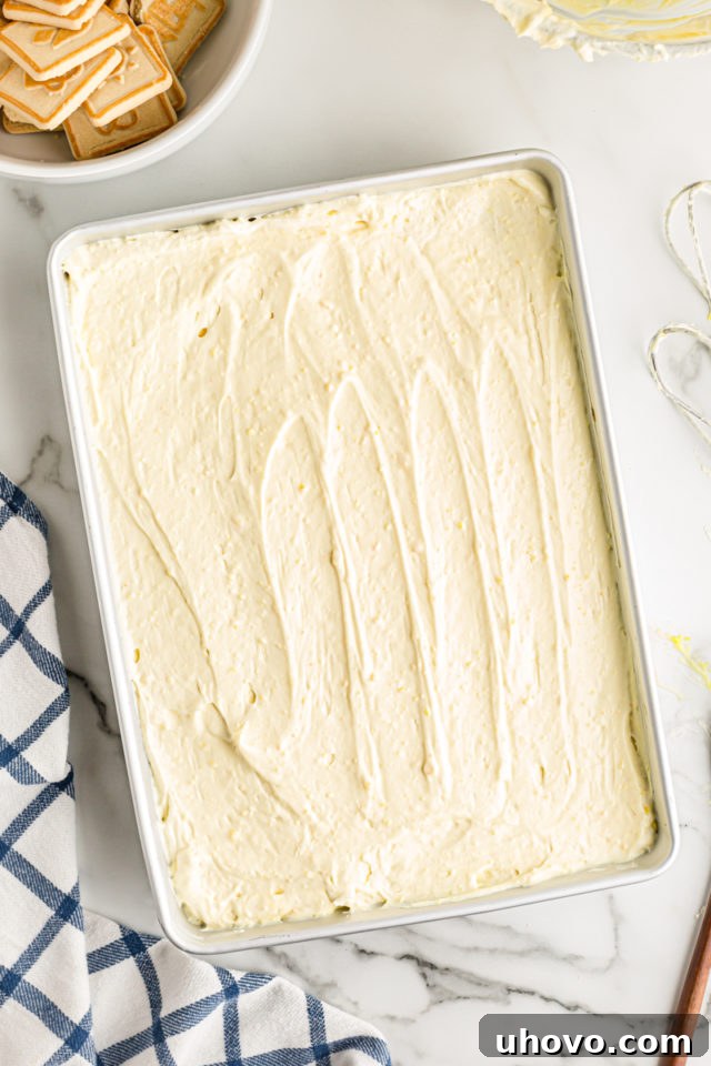 Overhead view of the creamy pudding mixture being spread evenly over the banana and cookie layers in the pan.