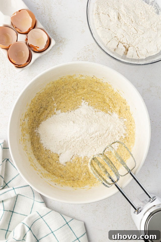 Overhead view of dry ingredients gradually added to wet ingredients for brown butter pound cake, showing a mixer at work.