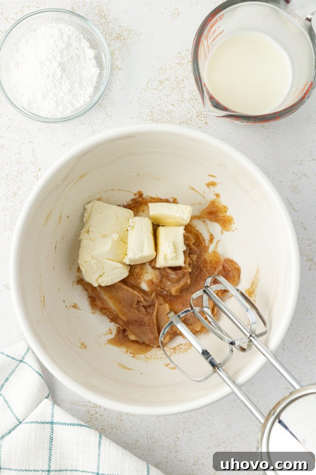 Overhead view of softened cream cheese and cooled brown butter in a mixing bowl, ready to be beaten for the glaze.