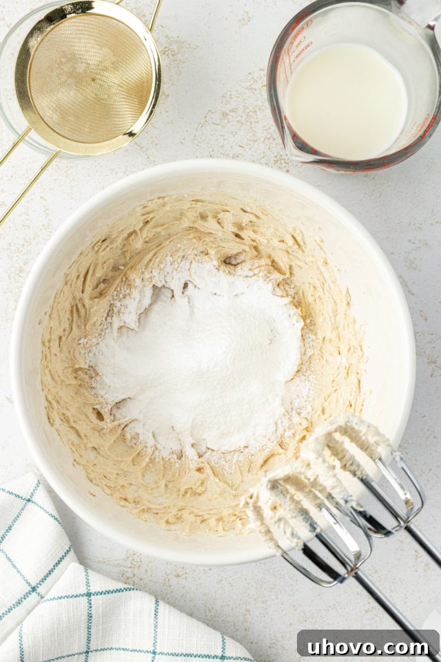 Overhead view of sifted confectioners' sugar being added to the butter-cream cheese mixture in a mixing bowl for the glaze.