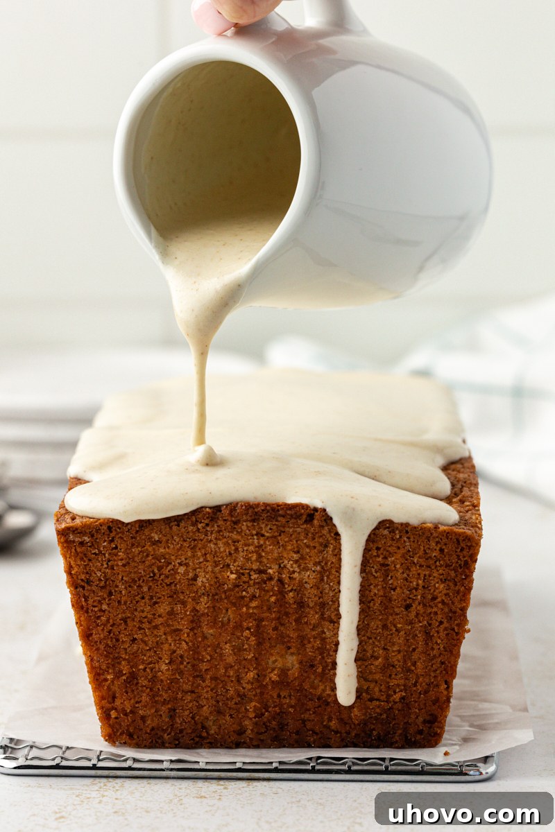 Brown butter cream cheese glaze being poured smoothly over a freshly baked brown butter pound cake, creating a beautiful coating.