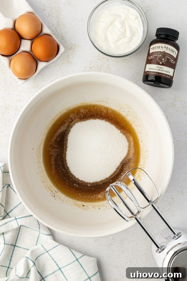 Overhead view of granulated sugar added to the cooled brown butter in a large mixing bowl.
