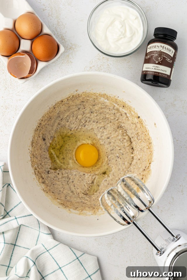 Overhead view of an egg being added to the mixed butter and sugar in a mixing bowl.