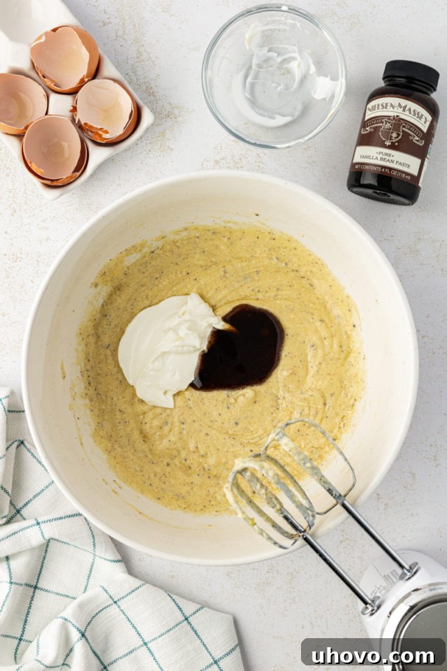 Overhead view of sour cream and vanilla bean paste being added to the cake batter.
