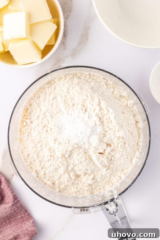 overhead view of flour and baking powder added to ground macadamias and sugar in the bowl of a food processor