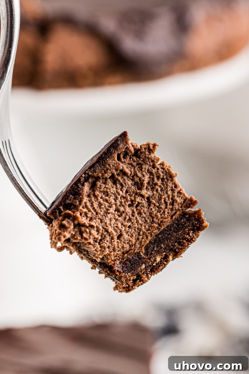 A close-up of a small bite of hazelnut mousse cake on the tip of a fork, showcasing the fluffy mousse and crisp crust.