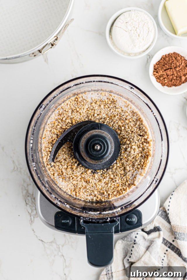 Close-up overhead view of finely chopped hazelnuts and sugar within a food processor, ready for the next ingredients.