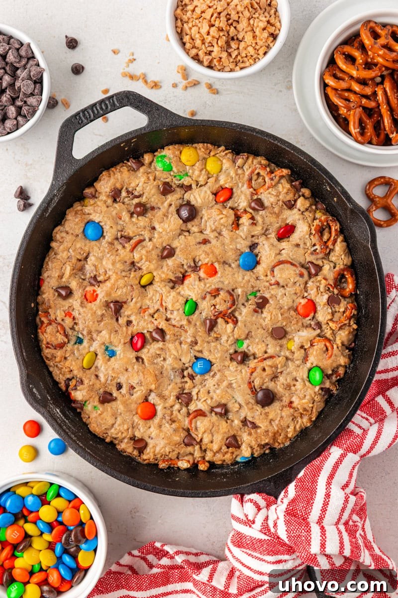 overhead view of monster skillet cookie on a white surface with small bowls of various add-ins surrounding