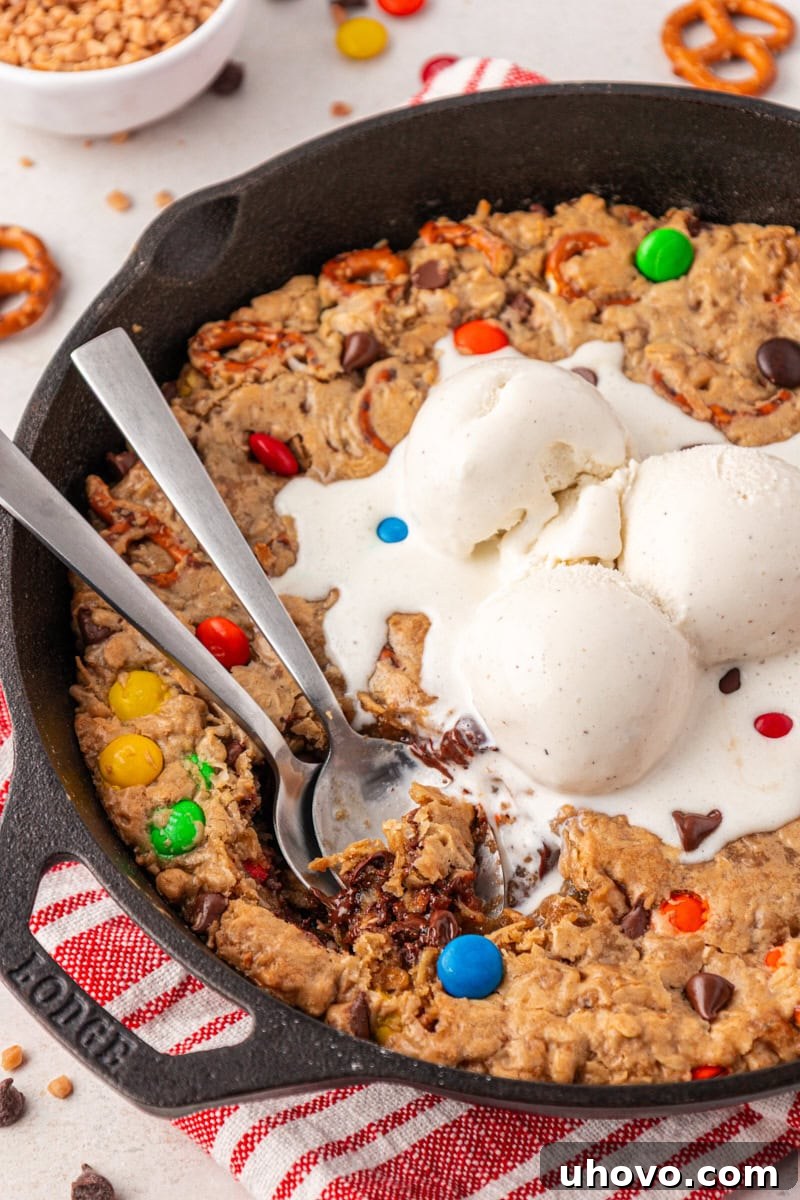 two spoons resting inside a skillet of monster skillet cookie topped with ice cream